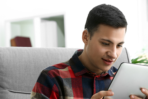 Young man with hearing aid using tablet computer at home