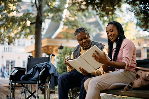 Senior adult with caretaker reading to him in the garden